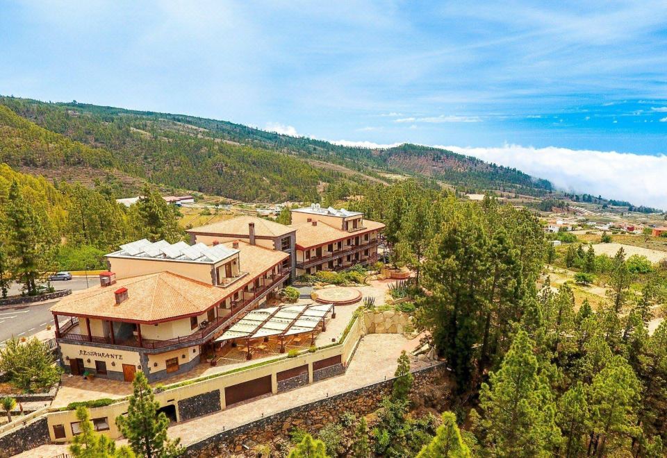 aerial view of a large hotel surrounded by trees and mountains , with a train traveling down the road at Hotel Spa Villalba