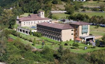 a large building with a brown roof is surrounded by greenery and trees , with people walking in the foreground at Parador de Cangas de Onis