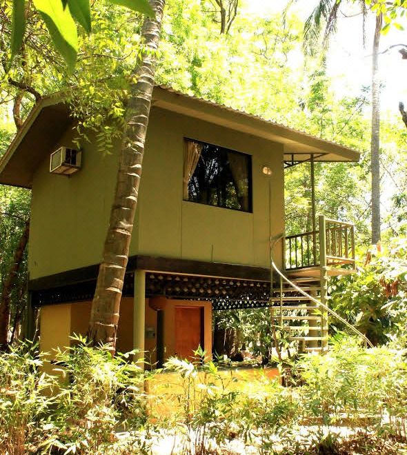 a small wooden house surrounded by trees and bushes , with a green roof and balcony at Puerto Barillas