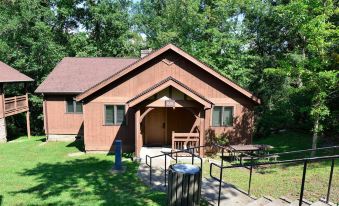 a brown wooden house surrounded by trees and grass , with benches and picnic tables outside at Cumberland Falls State Resort Park