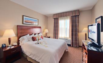 a large bed with white sheets and a wooden headboard is in a room with two lamps , a window , and a window seat at Hilton Garden Inn Laramie