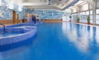 a large indoor swimming pool with blue tiles , surrounded by lounge chairs and a wall mural at Brandon House Hotel