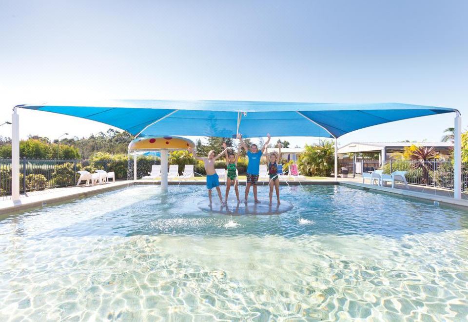 a group of people , including a man and a woman , are standing in a large swimming pool under a blue canopy , enjoying their time together at Nambucca River Village by Lincoln Place