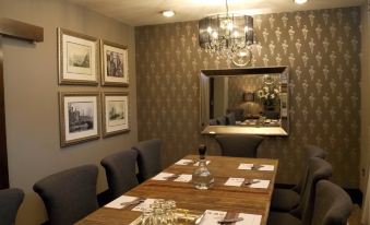 a long wooden table with multiple chairs and place settings in a room with patterned wallpaper at The Celtic Royal Hotel