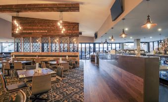 a restaurant with wooden tables and chairs , a bar area , and large windows overlooking the city at Mercure Warragul