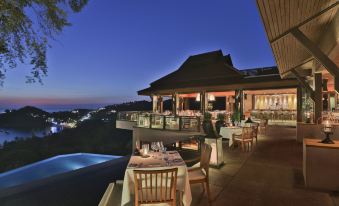 a nighttime view of an outdoor dining area with tables and chairs set up for a meal , overlooking a pool and the city at Pimalai Resort & Spa