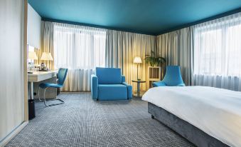 a modern hotel room with blue walls , white curtains , and a bed , as well as a living area with a couch and table at Park Inn by Radisson Krakow