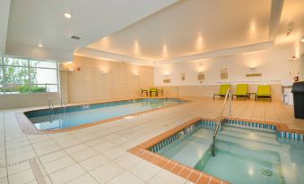an indoor swimming pool with a diving board and a hot tub , surrounded by chairs at SpringHill Suites Grand Forks