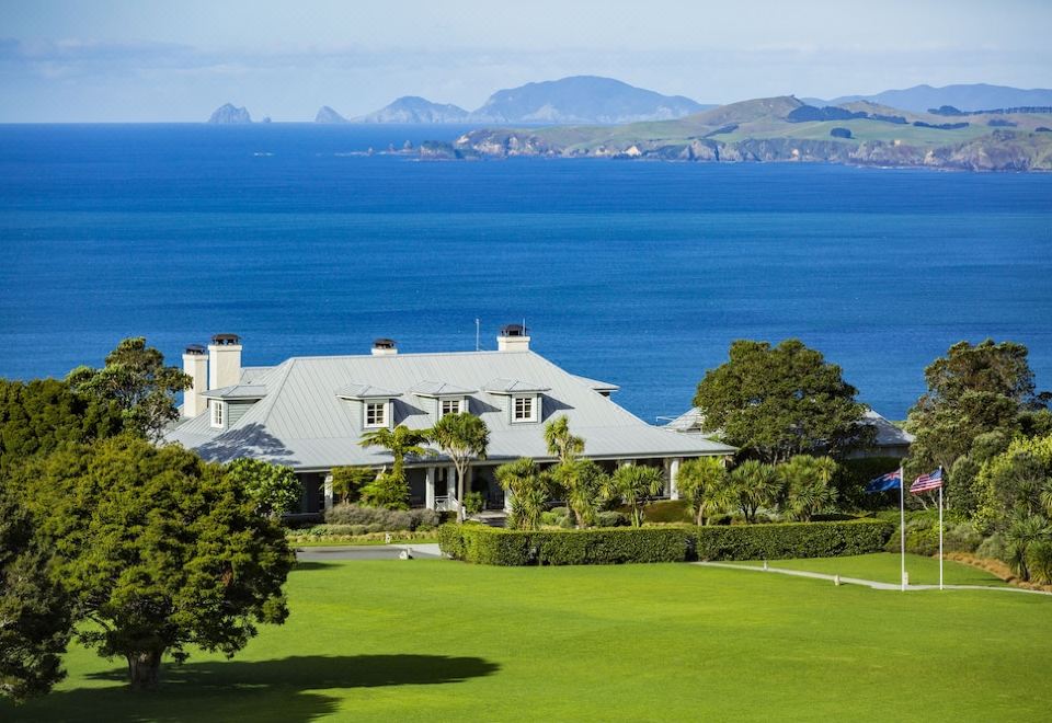 a large house with a white roof and green lawn is situated on the shore of the ocean at Rosewood Kauri Cliffs