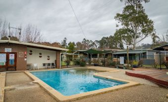 a backyard with a swimming pool surrounded by buildings , trees , and a clear blue sky at Big4 Breeze Holiday Parks - Eildon