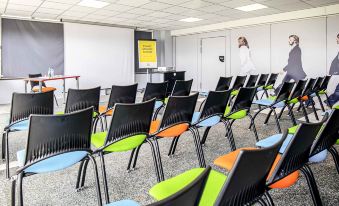 a conference room with rows of chairs arranged in a semicircle , and a projector screen on the wall at Ibis Styles Lille Marcq-en-Baroeul