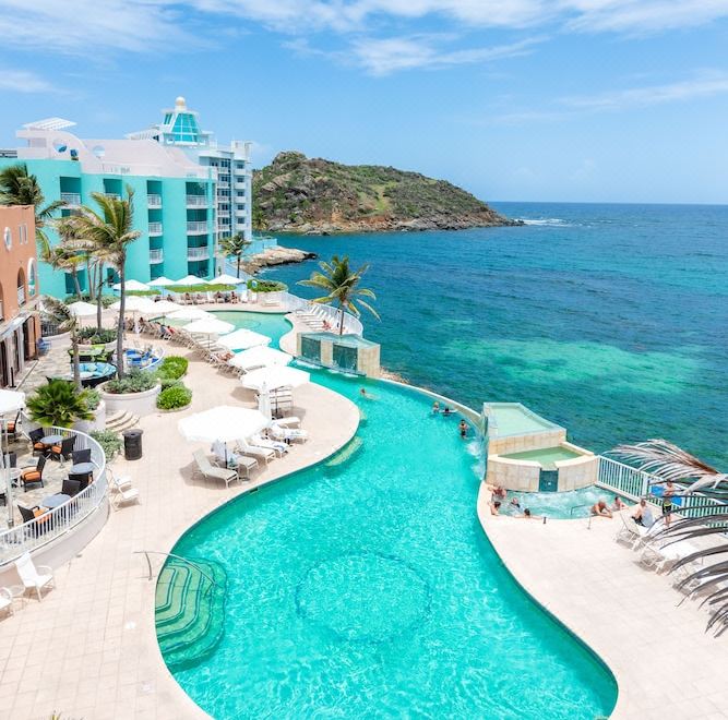 a luxurious beachfront resort with multiple swimming pools , umbrellas , and sun loungers , surrounded by clear blue water and green trees at Oyster Bay Beach Resort