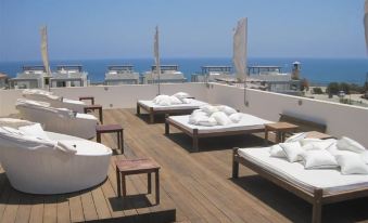a rooftop terrace with wooden decking , white lounge furniture , and umbrellas , offering a panoramic view of the ocean and sky at E-Hotel Larnaca Resort & Spa