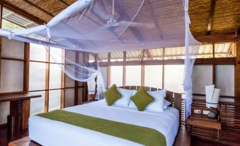 a large bed with a white and green comforter is in a room with wooden walls at Jicaro Island Lodge Member of the Cayuga Collection