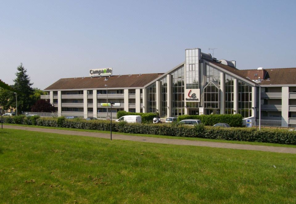 "a large , modern building with a glass facade and the words "" campagnolo "" on top is surrounded by greenery" at Campanile Marne la Vallee - Torcy