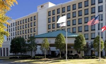 a large hotel with a flag flying in front of it , surrounded by trees and other buildings at DoubleTree by Hilton Atlanta Airport