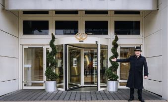 a man in a black coat stands outside of the sofitel hotel , with a large sign above the entrance at Sofitel London Gatwick