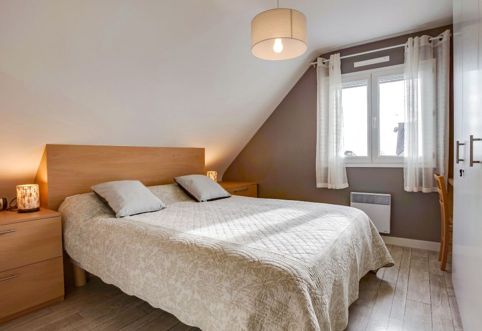 a cozy bedroom with a wooden bed , white sheets , and a window with curtains , under a sloping ceiling at L'Olivier