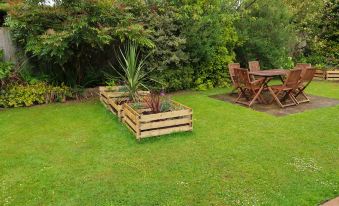 a lush green lawn with two wooden benches and a table , surrounded by trees and grass at Woodhouse Woodmancote