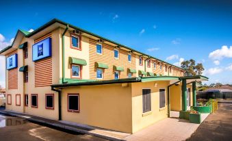 a yellow and green building with a blue sign on the side , situated in front of trees at ibis budget Casula Liverpool