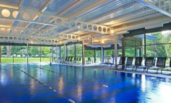 a large indoor swimming pool with blue water , surrounded by lounge chairs and a glass ceiling at Macdonald Berystede Hotel and Spa
