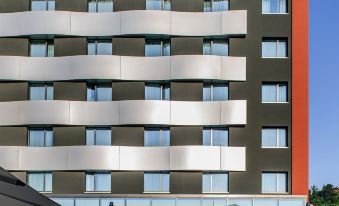 a modern building with a curved facade and multiple floors of windows , surrounded by white umbrellas and blue umbrellas at Novotel Lugano Paradiso