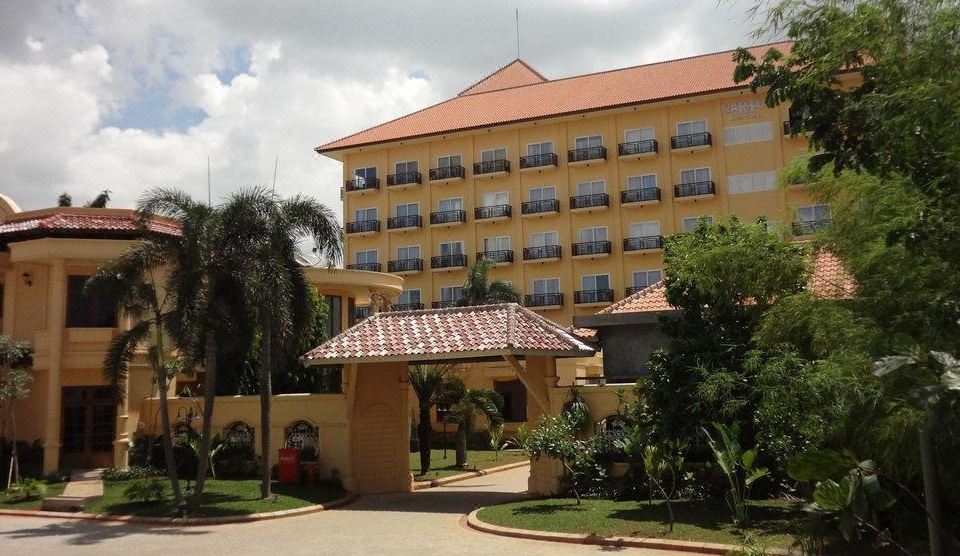 a large , yellow hotel building surrounded by a lush green lawn and palm trees , providing a picturesque setting at Narita Hotel Tangerang