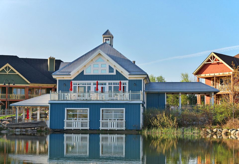 a blue house with a boat dock on the water , surrounded by trees and other buildings at Hilton Grand Vacations Club Blue Mountain Canada