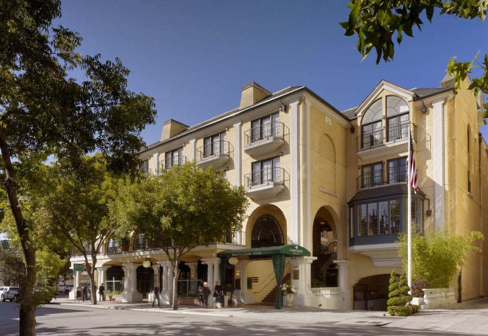 a large yellow building with a flagpole in front of it , surrounded by trees and people at El Prado