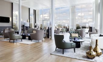 a modern , spacious living room with large windows and wooden floors , featuring comfortable seating arrangements and a dining area at AC Hotel Paris le Bourget Airport