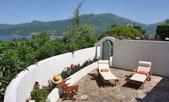 a patio with two lounge chairs , a bottle of wine , and a view of the ocean at A’mare Corsica Seaside Small Resort