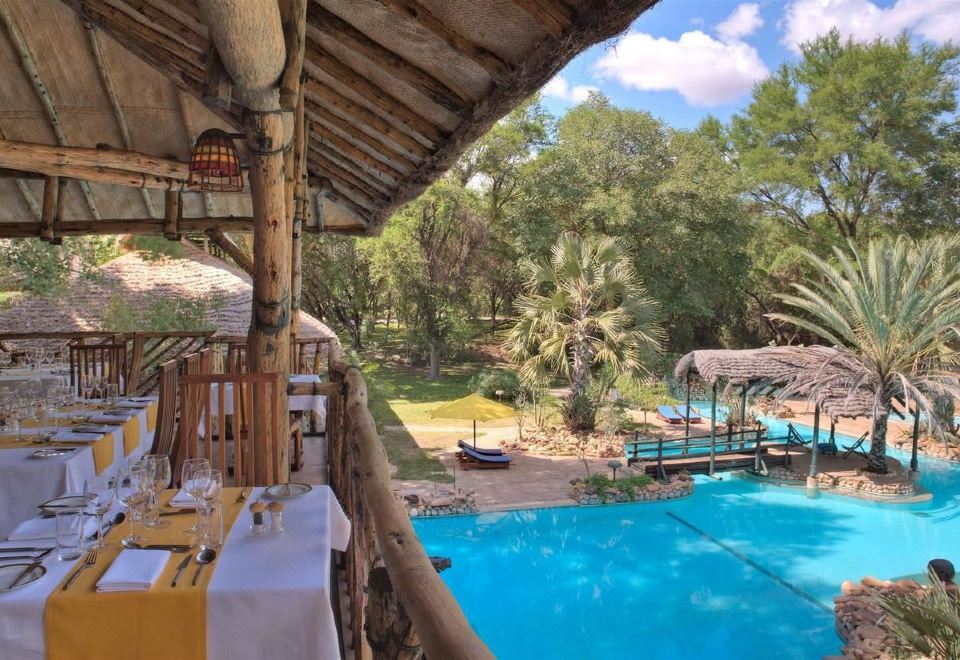 an outdoor dining area with a pool and umbrellas , surrounded by lush greenery and trees at Sarova Shaba Game Lodge