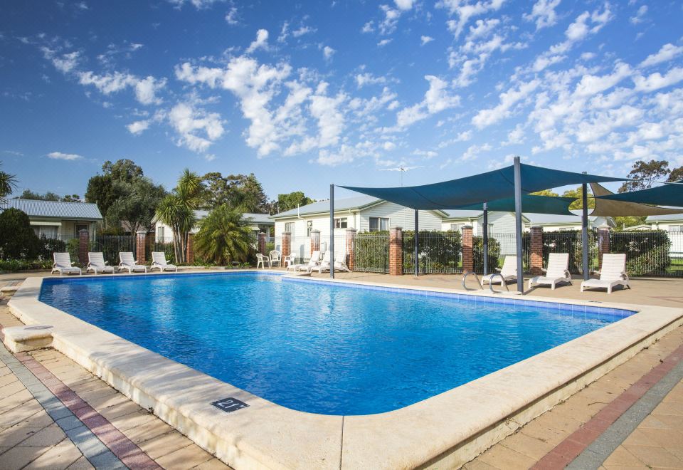 a large outdoor swimming pool surrounded by grass and trees , with several lounge chairs placed around it at Discovery Parks - Perth Airport