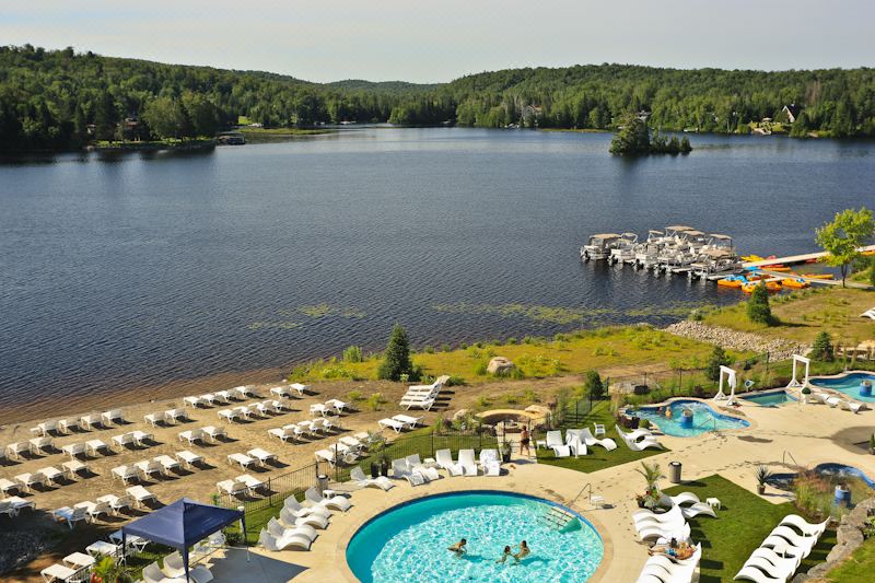 a large outdoor swimming pool surrounded by white lounge chairs and umbrellas , with a view of a lake and surrounding landscape at Estérel Resort