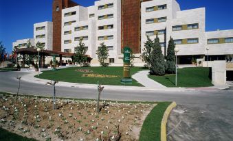 a large white building with a red roof and many windows is surrounded by a green garden at Parador de Salamanca