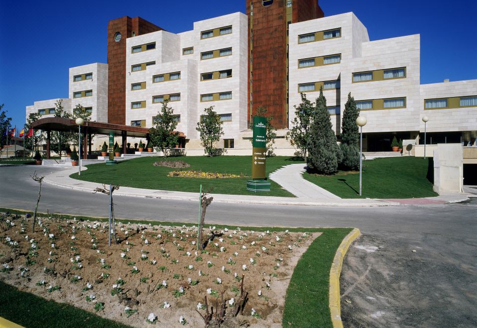 a large white building with a red roof and many windows is surrounded by a green garden at Parador de Salamanca