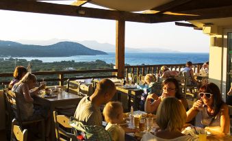 a group of people sitting at a dining table in a restaurant , enjoying a meal with a beautiful view of the ocean at Elpida Village