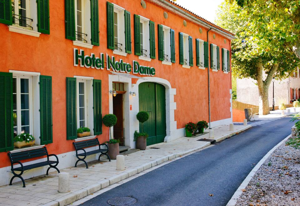 an orange building with green shutters and a bench in front of it , surrounded by trees at Hotel Restaurant Notre Dame