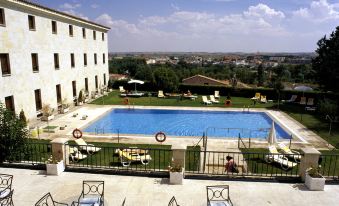a large outdoor swimming pool surrounded by lounge chairs and umbrellas , with a view of the city in the background at Parador de Zamora