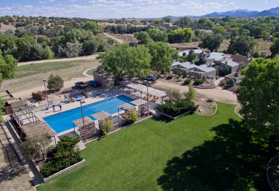 a large pool is surrounded by a grassy area and trees , with several buildings in the background at Ojo Santa Fe Spa Resort