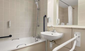 a modern bathroom with a white bathtub and sink , along with a mirror above the bathtub at Days Inn by Wyndham Sedgemoor M5