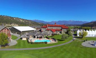 a large hotel with a red roof and a pool in front of it , surrounded by grass and mountains at St. Eugene Golf Resort & Casino
