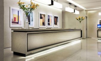 a modern hotel reception area with a large gray counter , white walls , and framed pictures on the wall at Paradise Hotel Busan