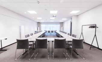 a long conference room with white walls , a large table surrounded by chairs , and a window providing natural light at Quality Hotel Winn Haninge