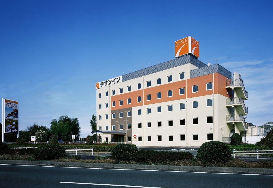 an orange and white hotel building with a large orange sign on the top , situated next to a road at Chisun Inn Munakata