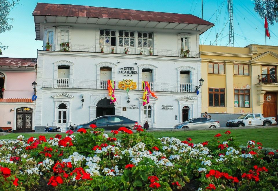 a white building with a red and white flag flying from it , surrounded by a lush green lawn and numerous potted plants at Hotel Casablanca