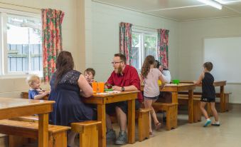 a group of people sitting at wooden tables in a room with floral curtains , engaged in conversation at Wellington Top 10 Holiday Park