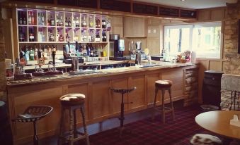 a bar with wooden cabinets and shelves filled with bottles , a window , and stools at the counter at The Twice Brewed Inn