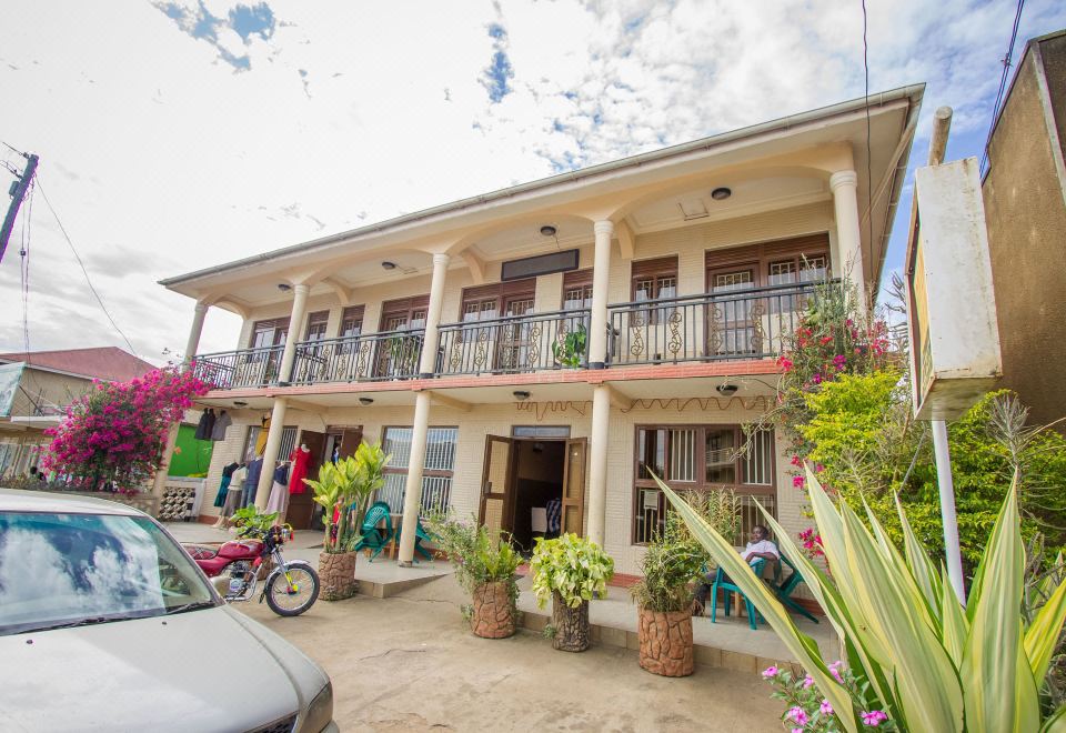 a two - story building with a balcony and potted plants on the front porch , surrounded by trees and a car parked in front of it at Collin Hotel