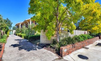 a large house with a brick wall and white picket fence is surrounded by trees and bushes at Lake Wendouree Luxury Apartments
